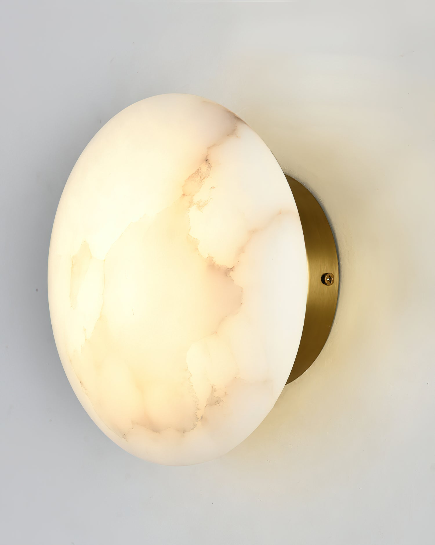 Angled close view of the Clérachic Alabaster Wall Sconce, brass backplate and fixing screw behind the lit stone.