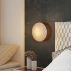 Clérachic Alabaster Wall Sconce lit against a dark bronze bedroom wall, beside a headboard and two ribbed vases.