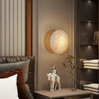 Clérachic Alabaster Wall Sconce above a bedside table in a panelled bedroom, casting a soft halo on the wall.