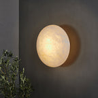 Clérachic Alabaster Wall Sconce on a charcoal wall with olive branches nearby, the stone lit from within.