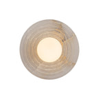 Lit face-on, the Clérachic alabaster sconce glows through the opal globe at its centre while the grey-veined stone rings stay soft.