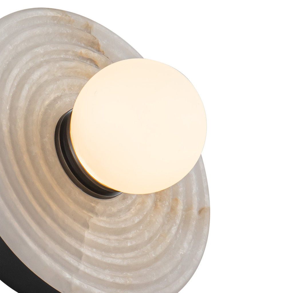 Close crop of the Clérachic alabaster sconce, the lit opal globe set against a black collar and the raw grain of the ribbed stone.