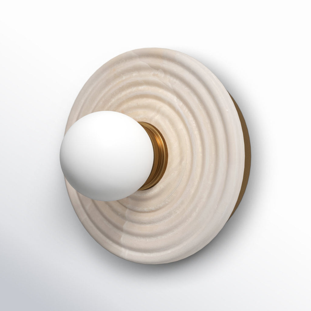 Angled study of the Clérachic alabaster sconce in gold, the opal globe pushed forward on a fluted brass collar over the ribbed stone.