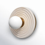 Angled study of the Clérachic alabaster sconce in gold, the opal globe pushed forward on a fluted brass collar over the ribbed stone.