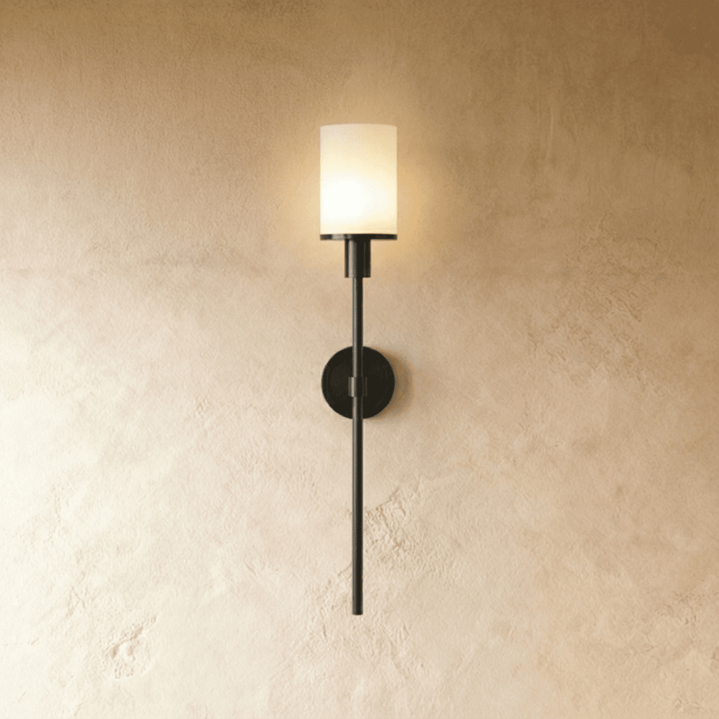 Clérachic slim black wall sconce with a lit white cylinder shade on a long rod, mounted on a warm limewash wall.