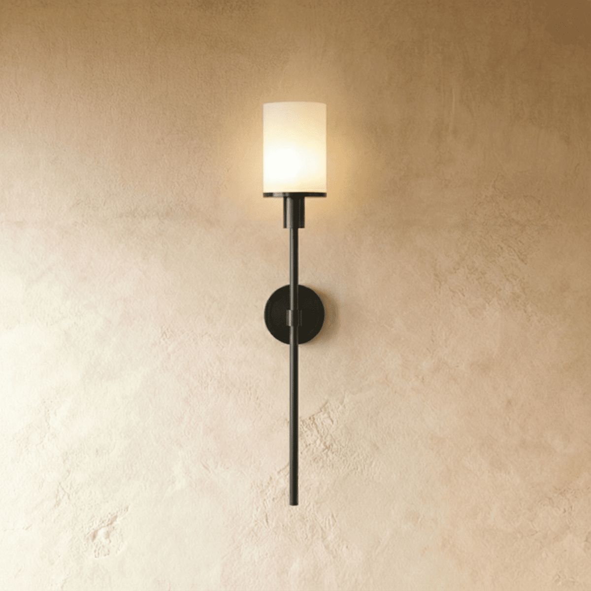 Clérachic slim black wall sconce with a lit white cylinder shade on a long rod, mounted on a warm limewash wall.