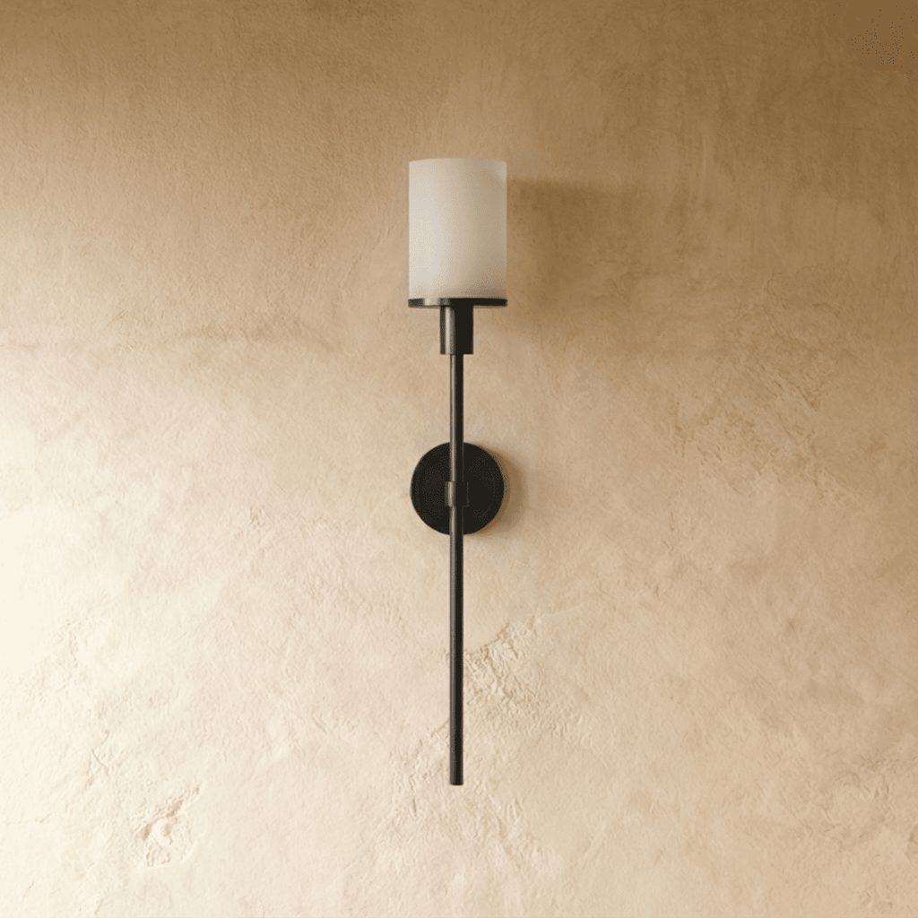 Clérachic black wall sconce with an unlit white cylinder shade, round backplate and long slim rod on limewash plaster.