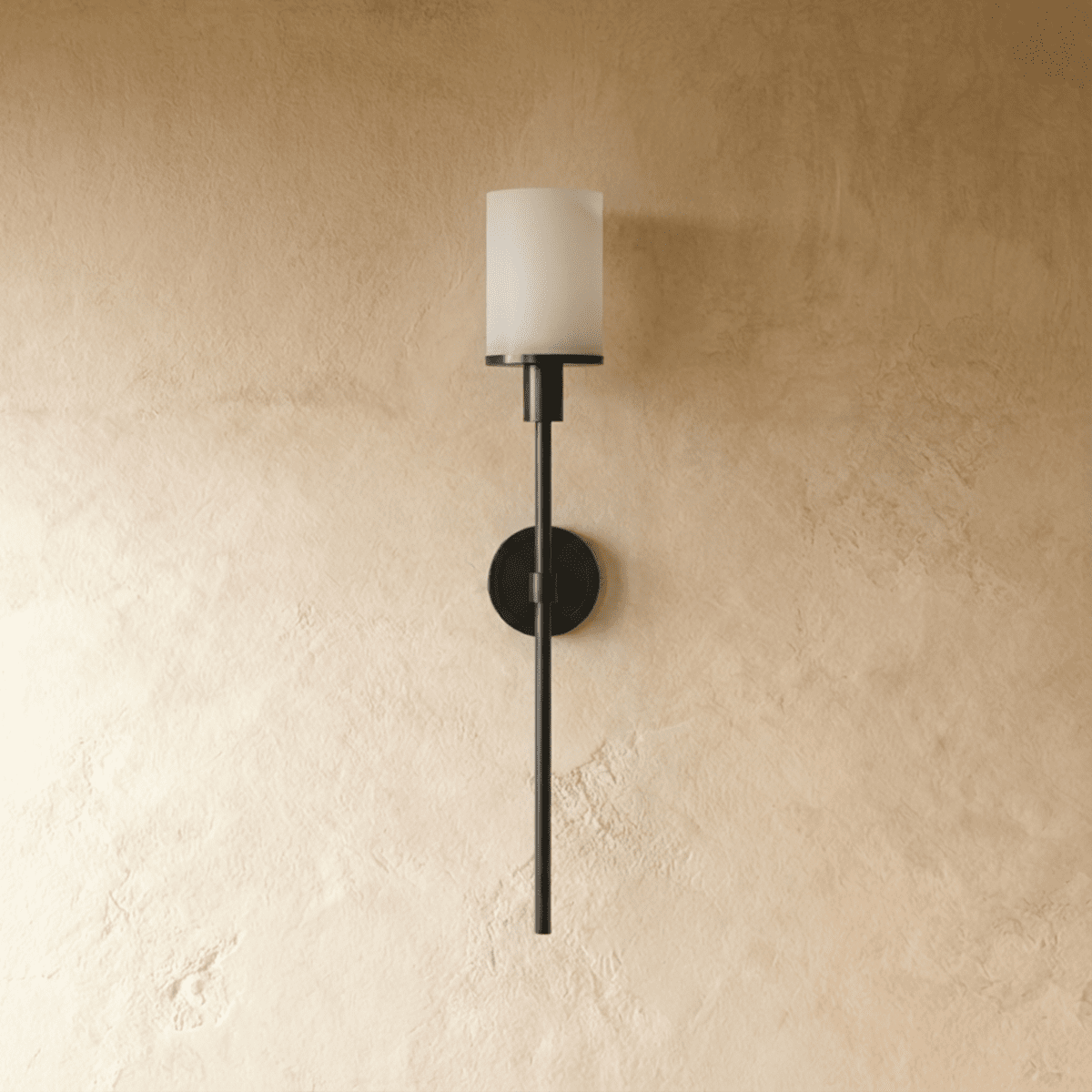 Clérachic black wall sconce with an unlit white cylinder shade, round backplate and long slim rod on limewash plaster.