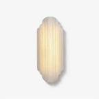 Front view of this Clérachic wall sconce on a plain white backdrop, a tall stepped alabaster shade glowing warm with soft vertical ribs.
