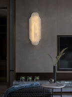 A lit Clérachic sconce on a dark wood wall above a low table with a tall vase and a blue throw, with a screen to the right.