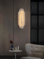 Clérachic alabaster sconce glowing on a wood-panelled wall, with a black-framed window and a small round table below.