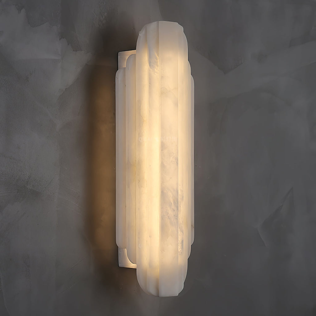 Three-quarter view of this Clérachic alabaster sconce lit on a dark grey wall, showing the ribbed shade and the slim metal back plate.