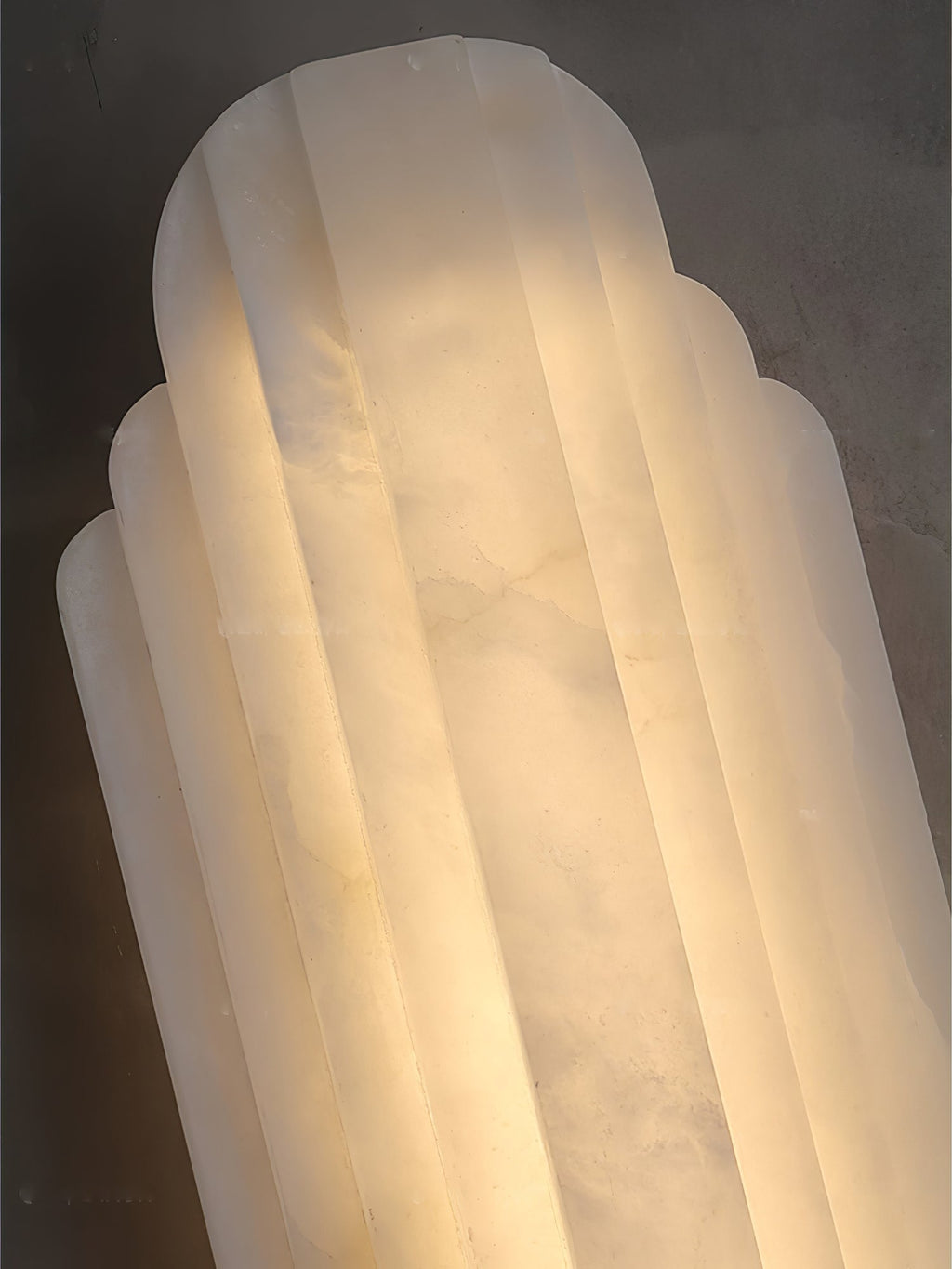 Close view of the top of this Clérachic alabaster sconce, showing its stepped, ribbed shade lit from inside.