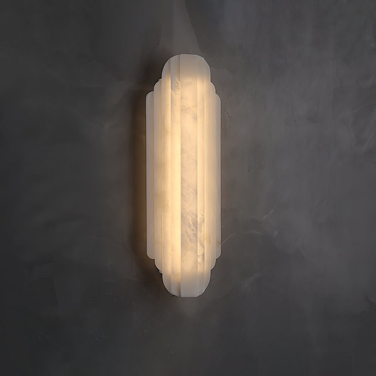 A Clérachic alabaster sconce lit on a dark grey plaster wall, its ribbed shade glowing with soft veining visible in the stone.