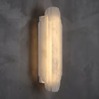 Three-quarter view of this Clérachic alabaster sconce lit on a dark grey wall, with the slim white back plate visible behind the shade.