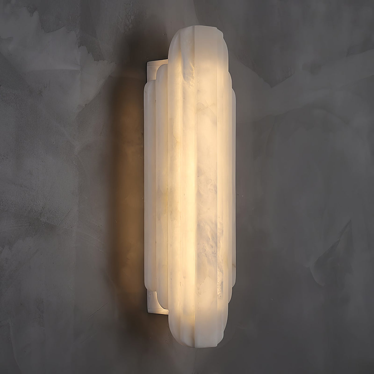 Three-quarter view of this Clérachic alabaster sconce lit on a dark grey wall, with the slim white back plate visible behind the shade.