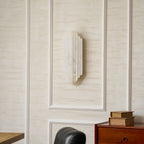 An unlit Clérachic alabaster sconce on a cream panelled wall, its pale ribbed shade above a stack of books on a wooden chest.