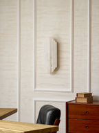 The unlit Clérachic alabaster sconce on a panelled wall, with a black leather chair and a chest of drawers below it.