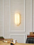 A lit Clérachic alabaster sconce glowing warm on a panelled cream wall, above a desk with an open book and a white cup.