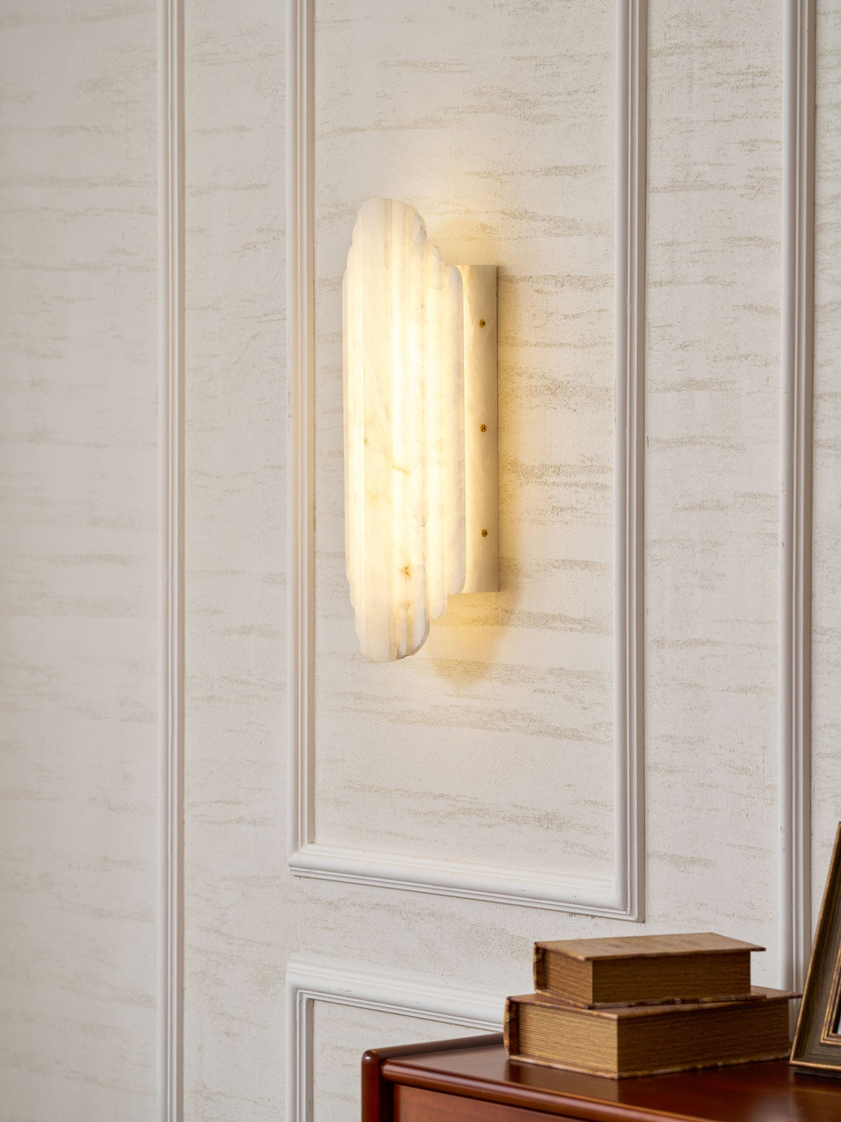 Three-quarter view of the lit Clérachic alabaster sconce on a panelled wall, its ribbed shade glowing beside the wall plate.