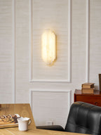 A lit Clérachic alabaster sconce on a panelled wall, with a desk, an open book, a cup and a black leather chair below.