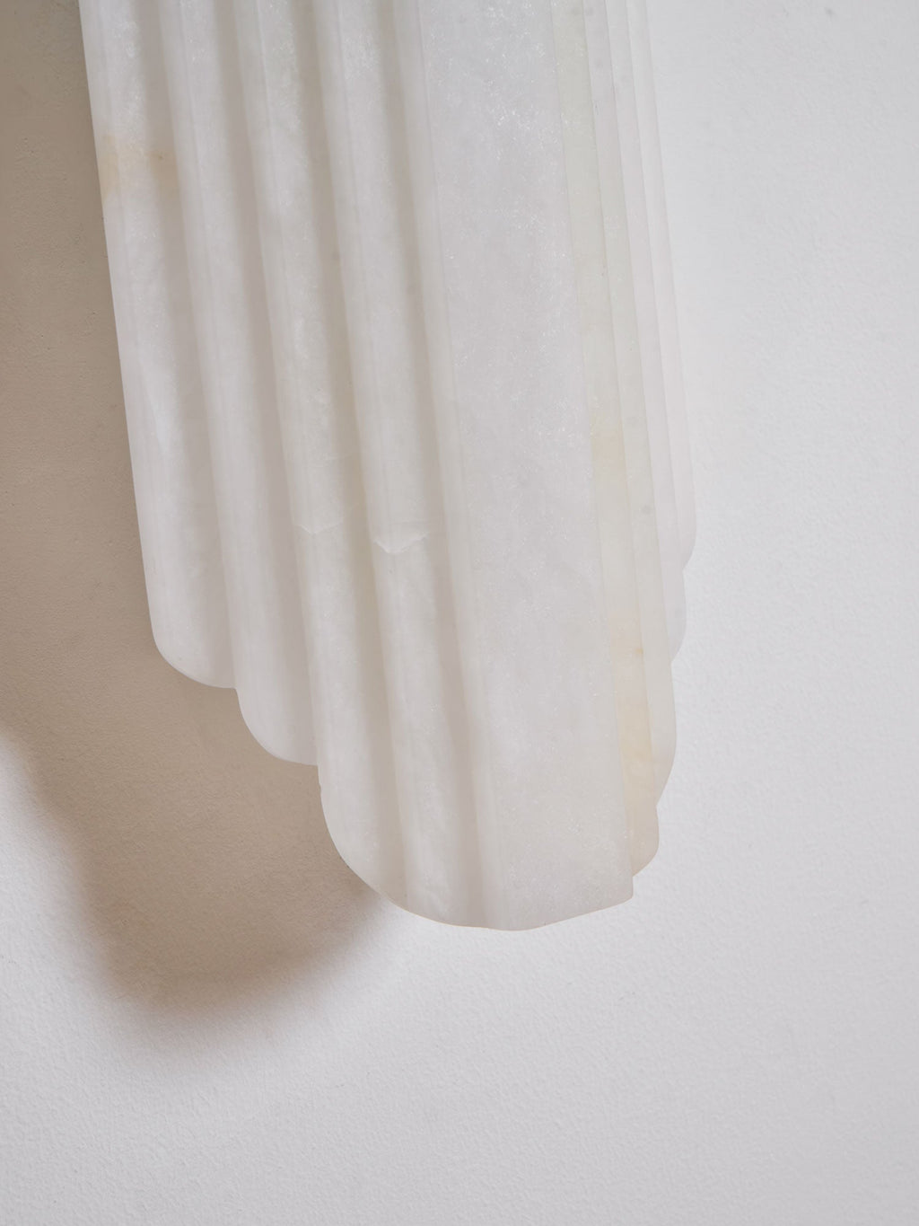 Close view of the lower edge of this Clérachic alabaster sconce, showing the stepped, ribbed stone against a white wall.
