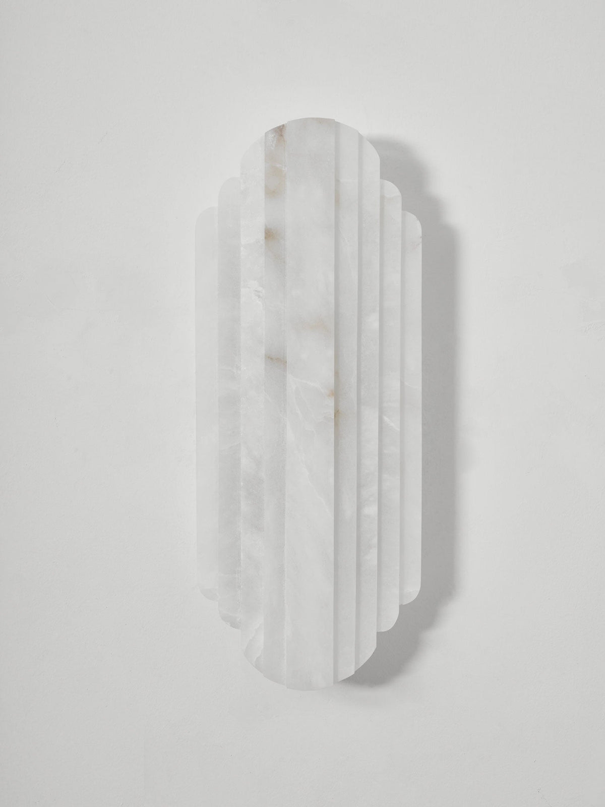 Front view of the unlit Clérachic alabaster sconce on a pale grey wall, showing the white, lightly veined ribs of the stone.
