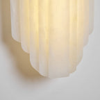 Close view of the stepped lower edge of the lit Clérachic alabaster sconce, glowing warm against a pale wall.