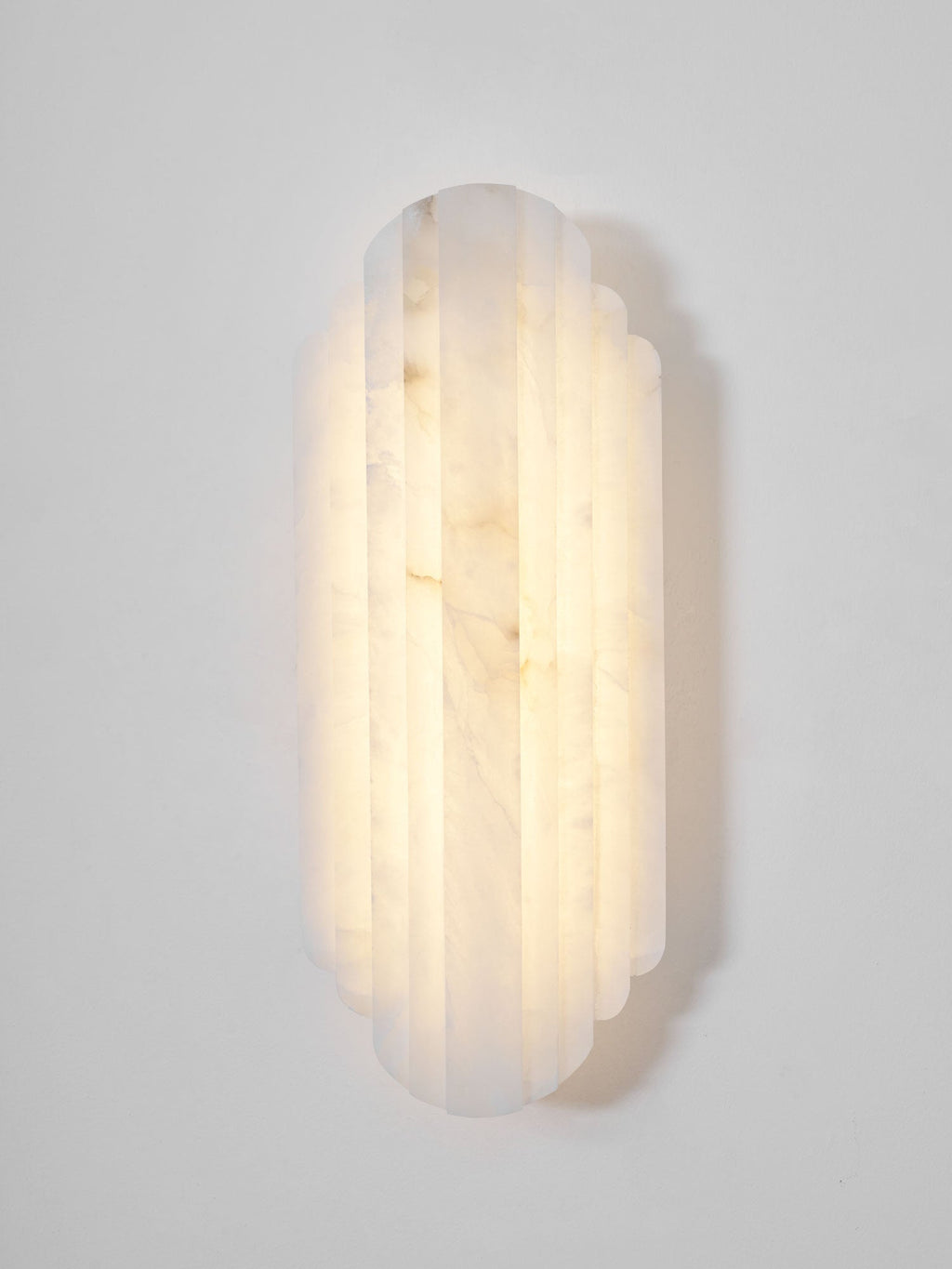 Close front view of the lit Clérachic alabaster sconce, its ribbed shade glowing warm with soft brown veining.