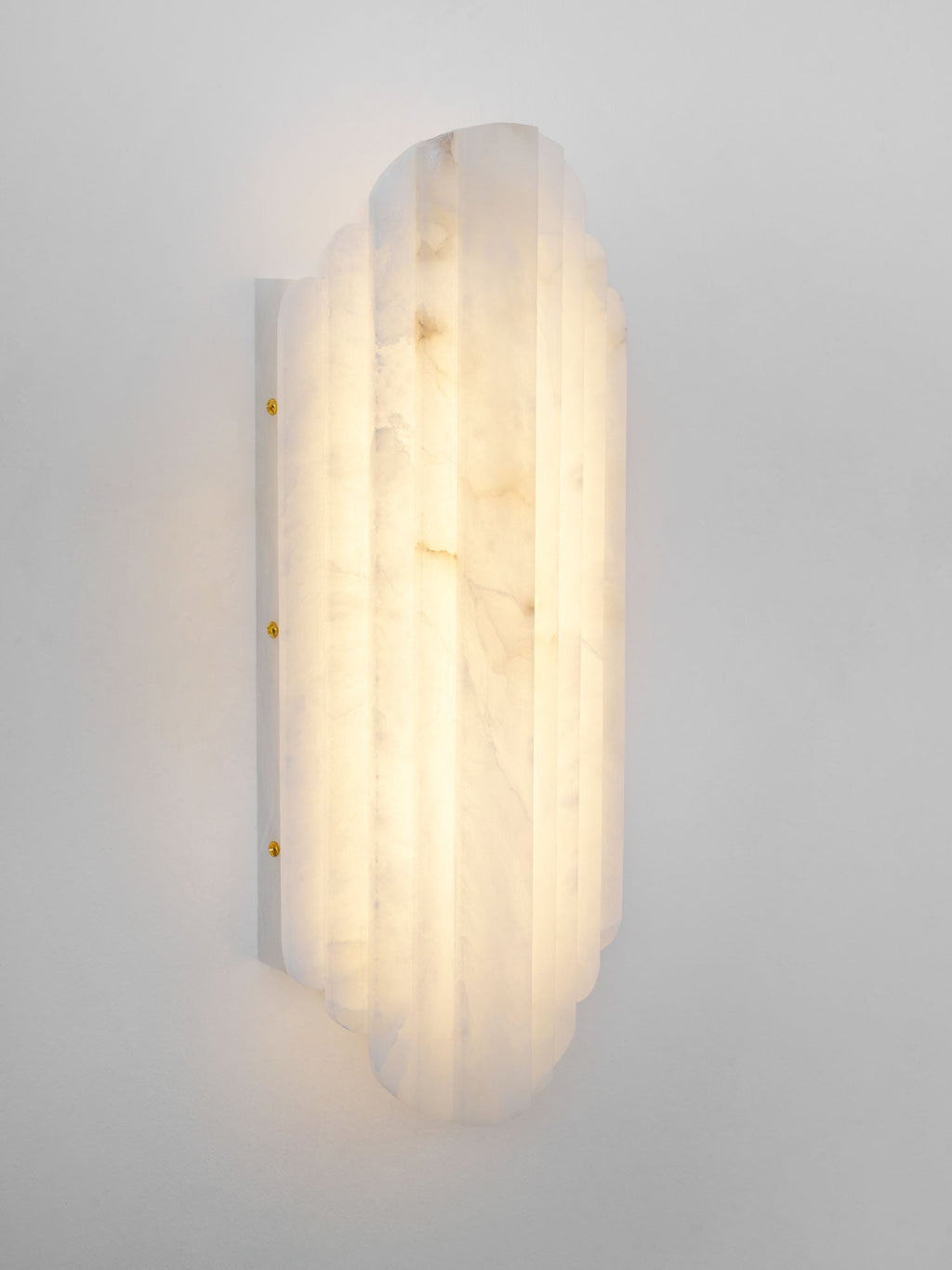 Three-quarter view of the lit Clérachic alabaster sconce, showing the ribbed shade, the veining and the brass-coloured screws on its plate.