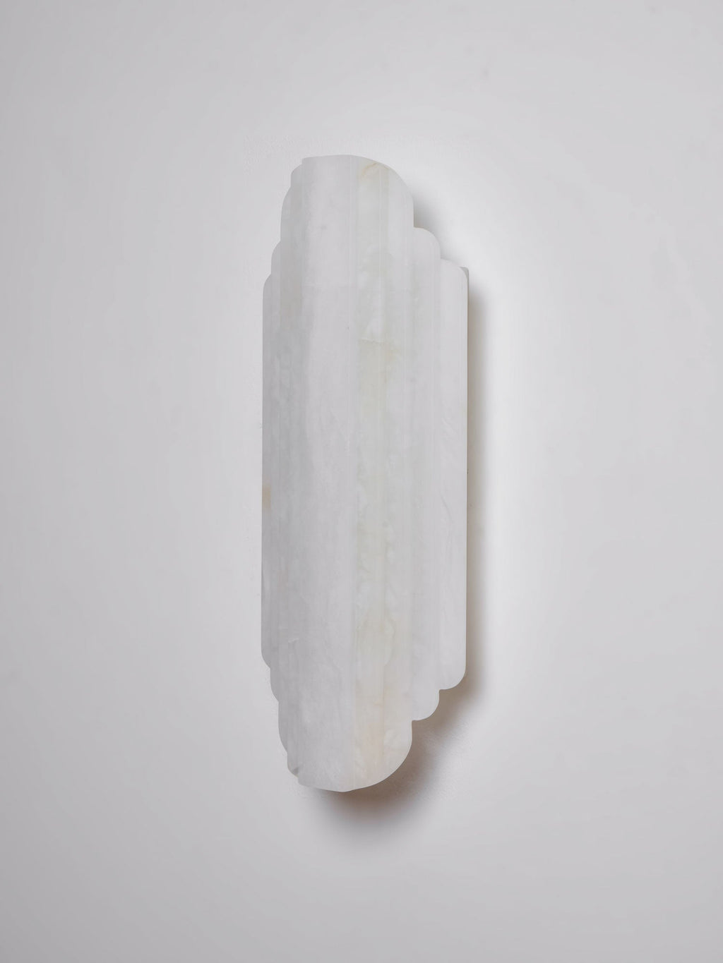 Three-quarter view of the unlit Clérachic alabaster sconce on a pale grey wall, its white stone ribs lightly veined.