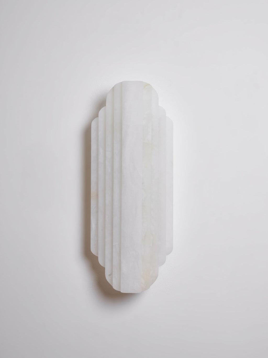 A shorter, unlit Clérachic alabaster sconce on a pale wall, its stepped white ribs in a soft shadow.