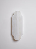 A shorter, unlit Clérachic alabaster sconce on a pale wall, its stepped white ribs in a soft shadow.