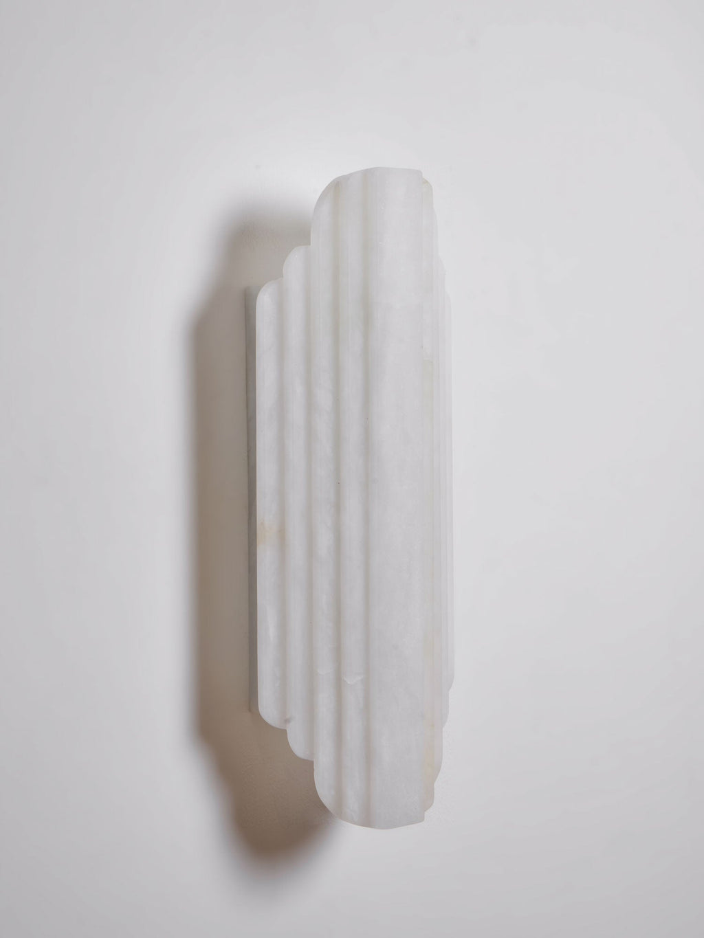Three-quarter view of the shorter, unlit Clérachic alabaster sconce, showing its stepped ribs and the shadow it casts on the wall.