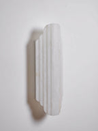 Three-quarter view of the shorter, unlit Clérachic alabaster sconce, showing its stepped ribs and the shadow it casts on the wall.