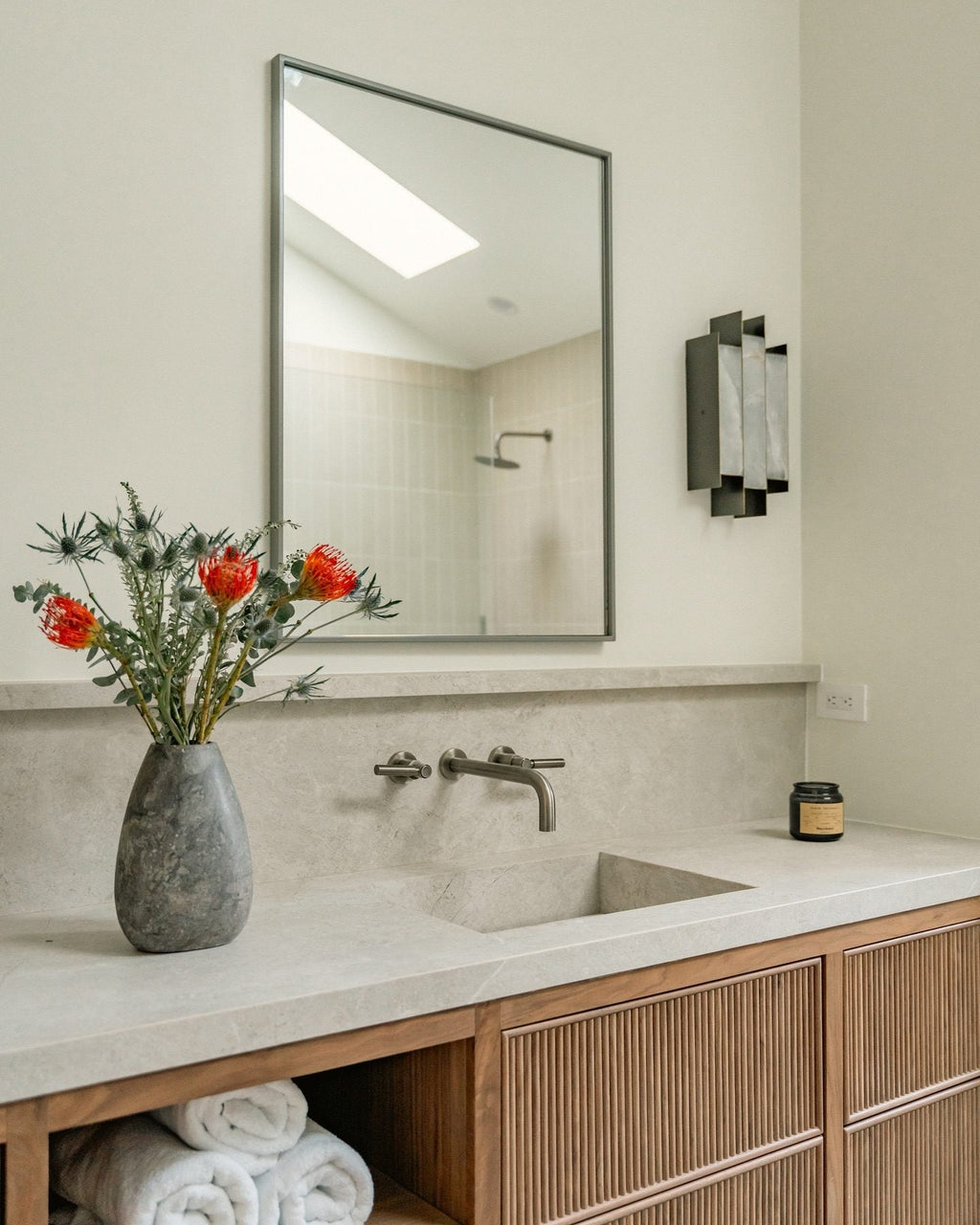 Clérachic Alabaster Wall Sconce beside a mirror above a stone-topped washstand, its stepped blades dark against pale plaster.