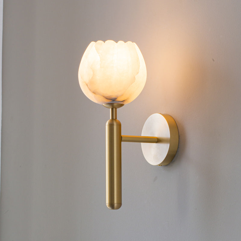 Clérachic alabaster wall sconce in brushed brass, its scalloped tulip shade lit and washing warm light up a pale grey wall.