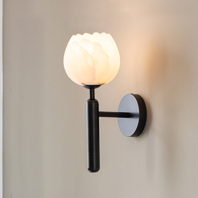 The Clérachic alabaster wall sconce in matte black, its tulip shade glowing against a soft greige wall with warm light behind it.