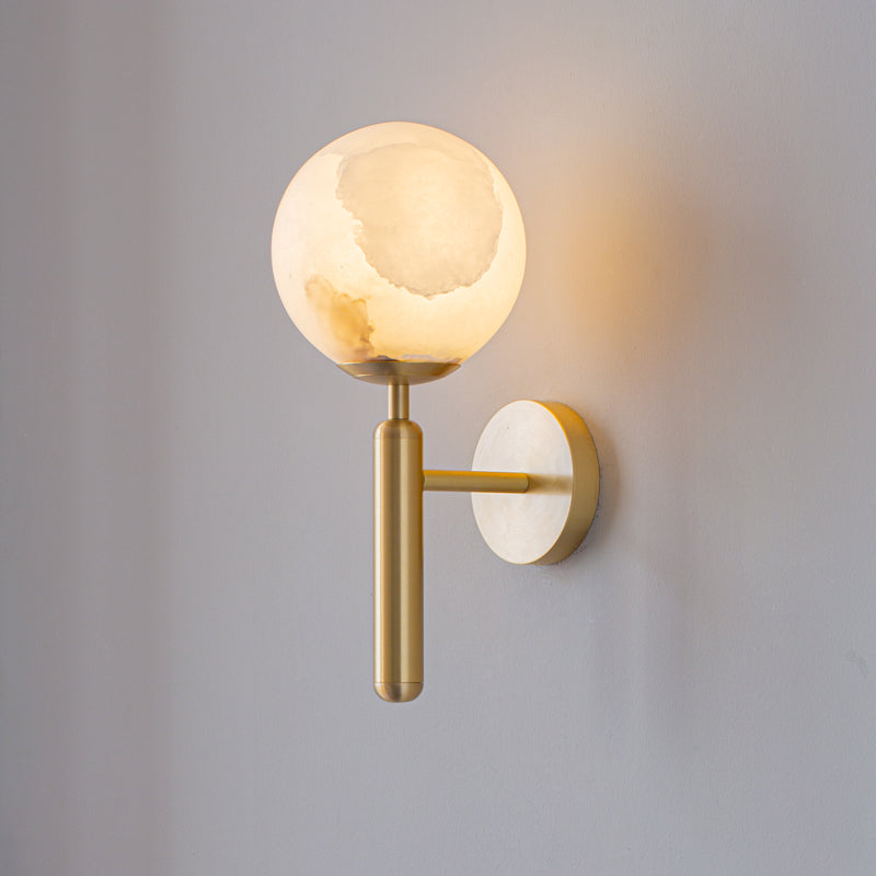 Brushed brass Clérachic alabaster wall sconce with the plain globe shade, the stone's amber veining showing as it glows.