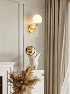Clérachic alabaster wall sconce in brass, globe shade lit on a cream moulded wall above a mantel of dried pampas grass.