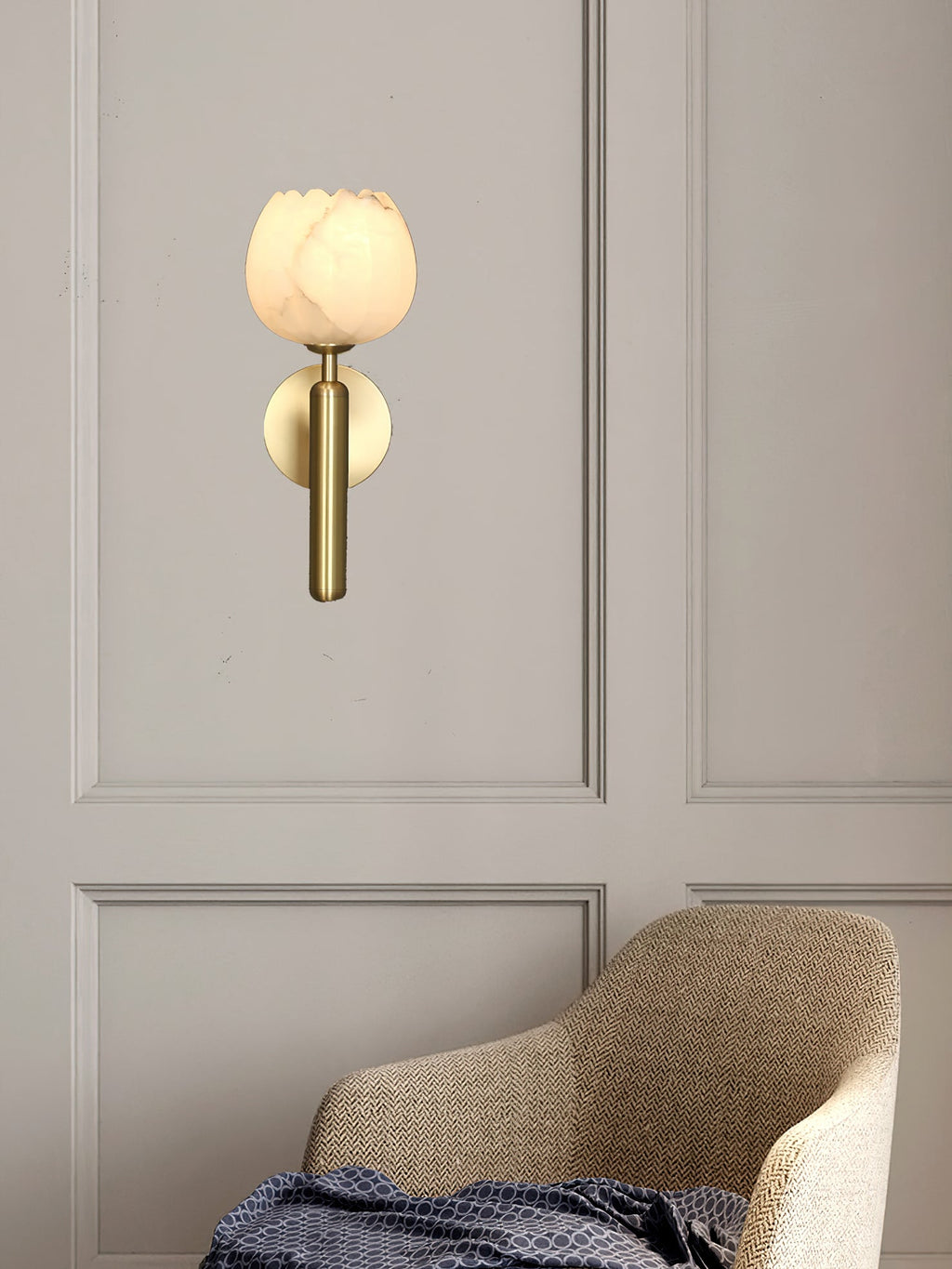 Brass Clérachic alabaster wall sconce with the tulip shade above a herringbone armchair on a panelled greige wall.