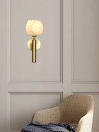 Brass Clérachic alabaster wall sconce with the tulip shade above a herringbone armchair on a panelled greige wall.