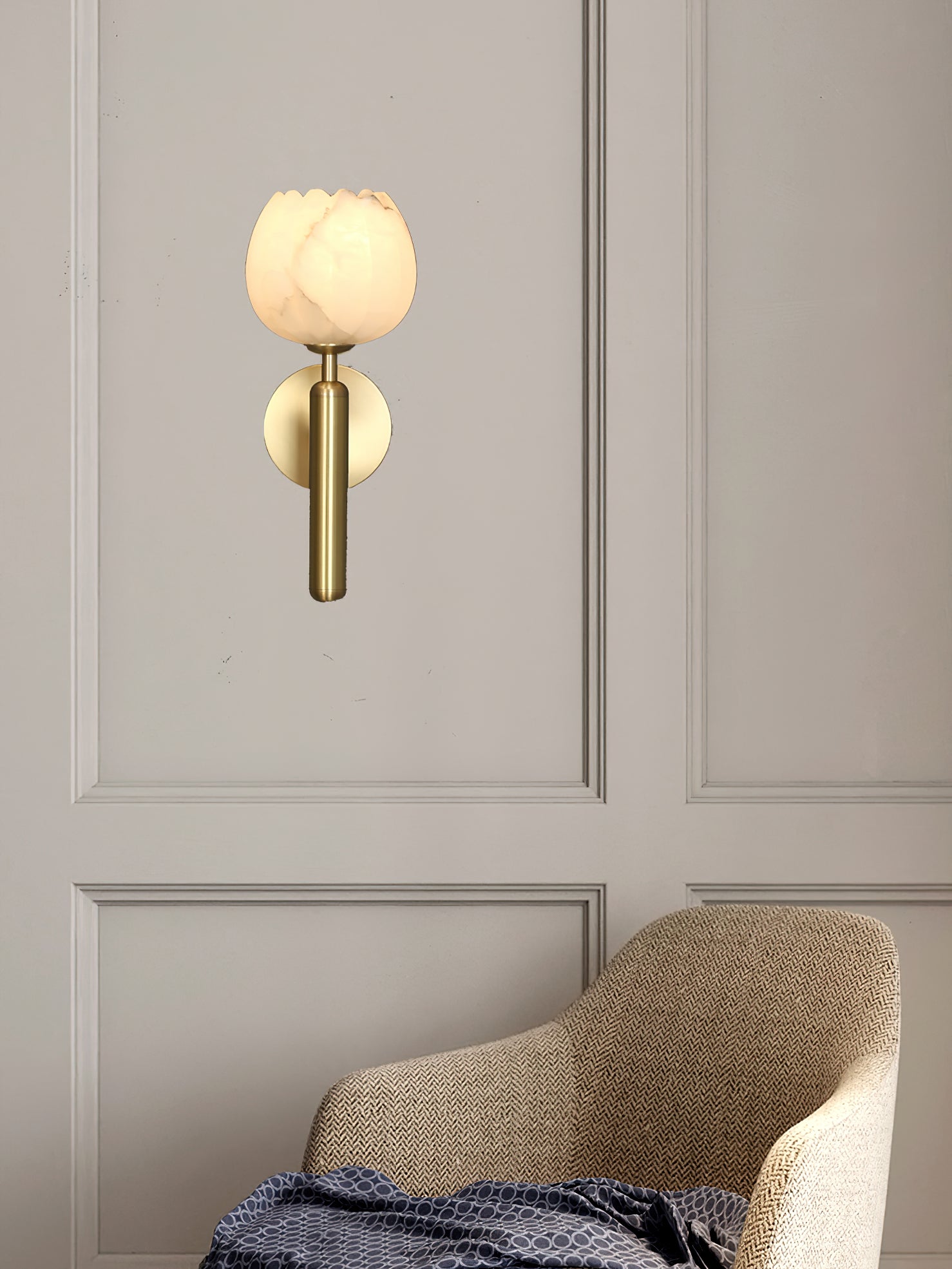 Brass Clérachic alabaster wall sconce with the tulip shade above a herringbone armchair on a panelled greige wall.