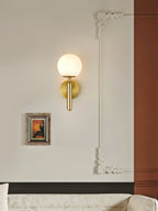 The Clérachic alabaster wall sconce in brass lights a cream drawing-room wall beside a small framed painting and moulding.