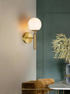 Clérachic alabaster wall sconce in brass on a corner wall, globe shade lit beside a deep green panel and gold dried stems.