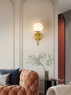 Brass Clérachic alabaster wall sconce above a tufted terracotta sofa, globe shade lit on an ornate panelled cream wall.
