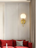 Brass Clérachic alabaster wall sconce glowing on a panelled wall above a deep red velvet sofa and a gingham cushion.