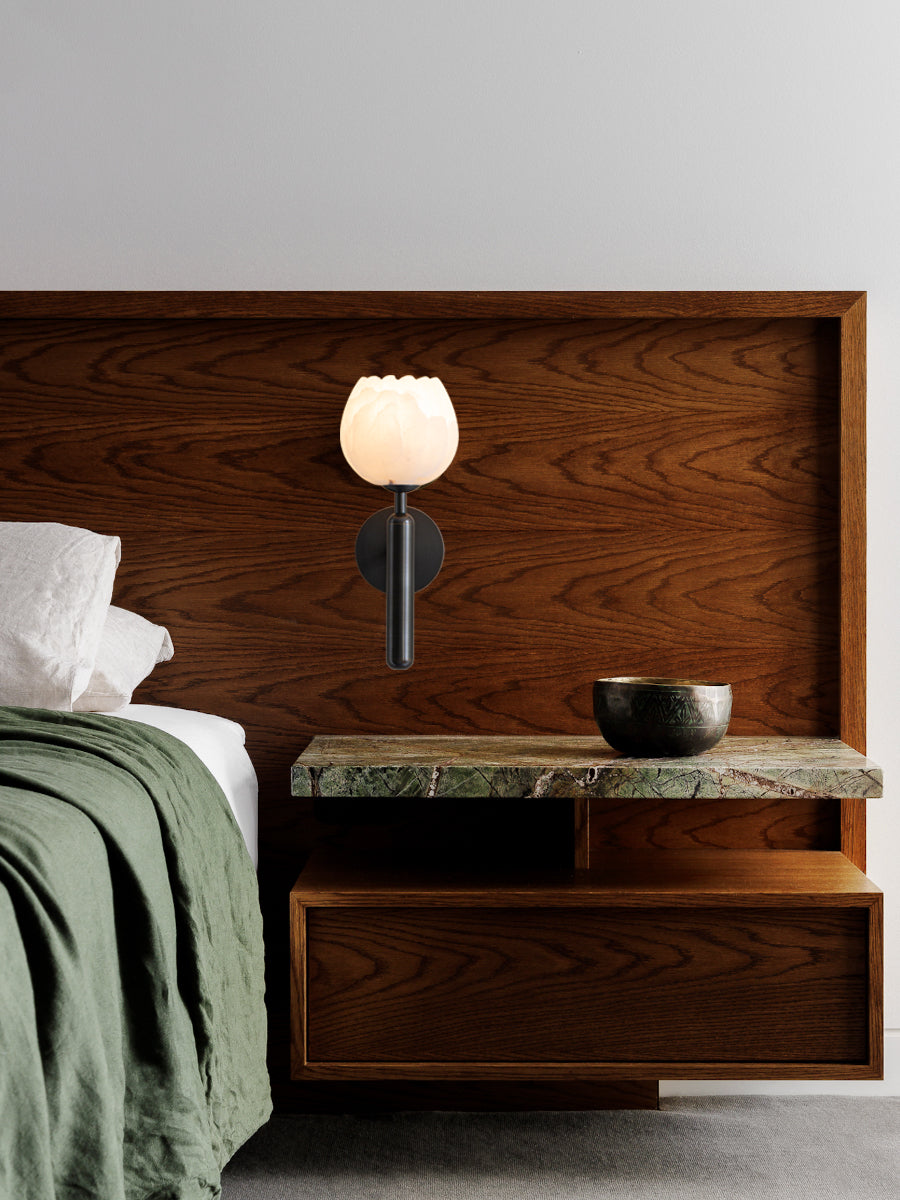 Black Clérachic alabaster wall sconce fitted to a walnut headboard panel above a green marble shelf and a brass bowl.