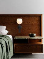Black Clérachic alabaster wall sconce fitted to a walnut headboard panel above a green marble shelf and a brass bowl.