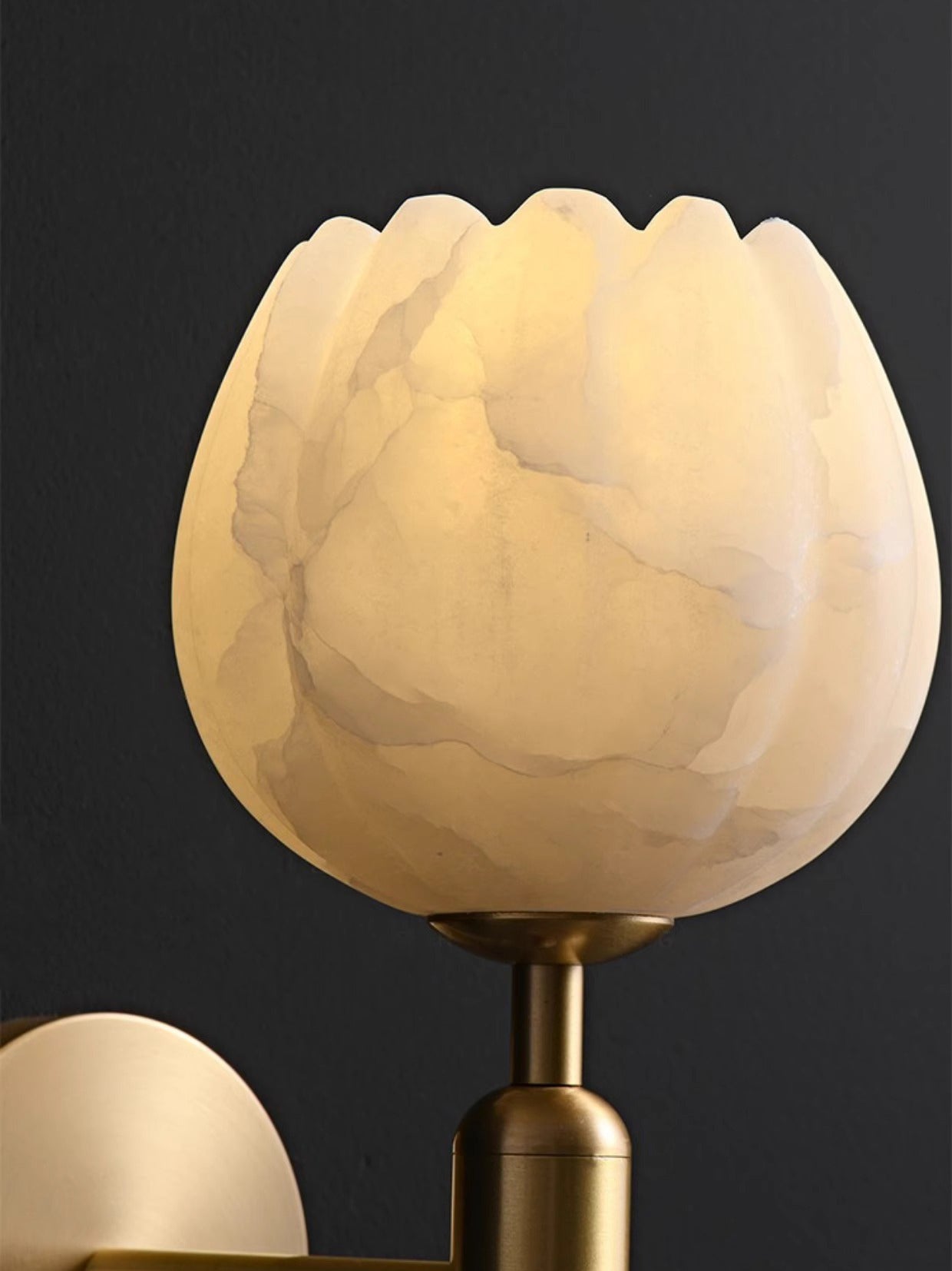 Close-up of the Clérachic alabaster wall sconce shade, its scalloped rim and grey-amber veining lit from within.